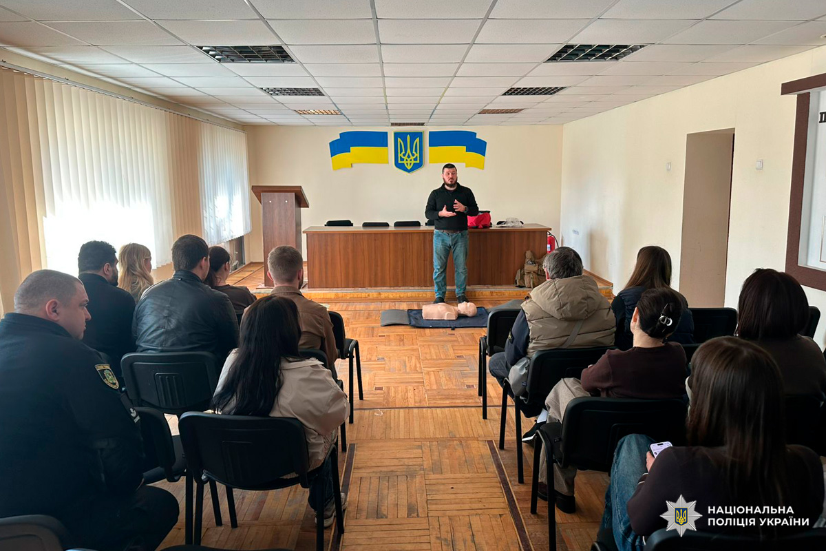 Група слухачів бере участь у занятті з серцево‑легеневої реанімації, інструктор демонструє процедуру на манекені.