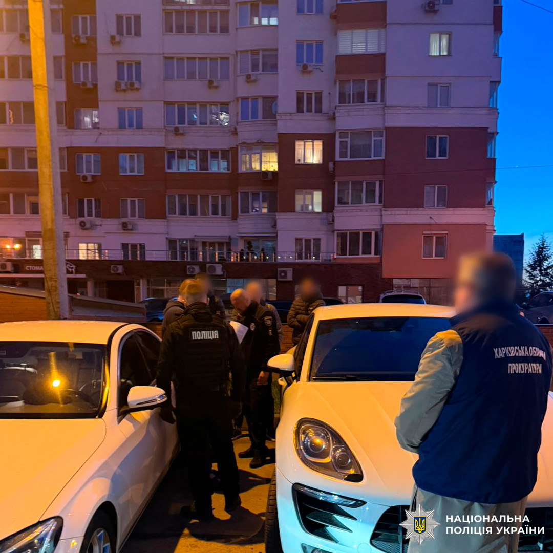 Група правоохоронців у формі між двома автомобілями, поруч багатоповерхівка,