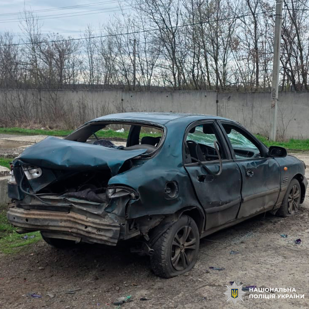 Темний седан із серйозними пошкодженнями задньої частини, розбитим склом та деформованим багажником, зафіксований на ґрунтовій дорозі біля бетонної стіни.