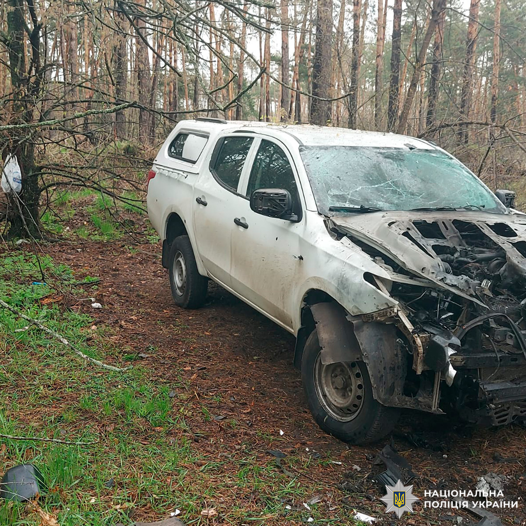 Білий пікап із серйозними пошкодженнями передньої частини, розбитим лобовим склом та відсутнім капотом, зафіксований на лісовій доріжці.
