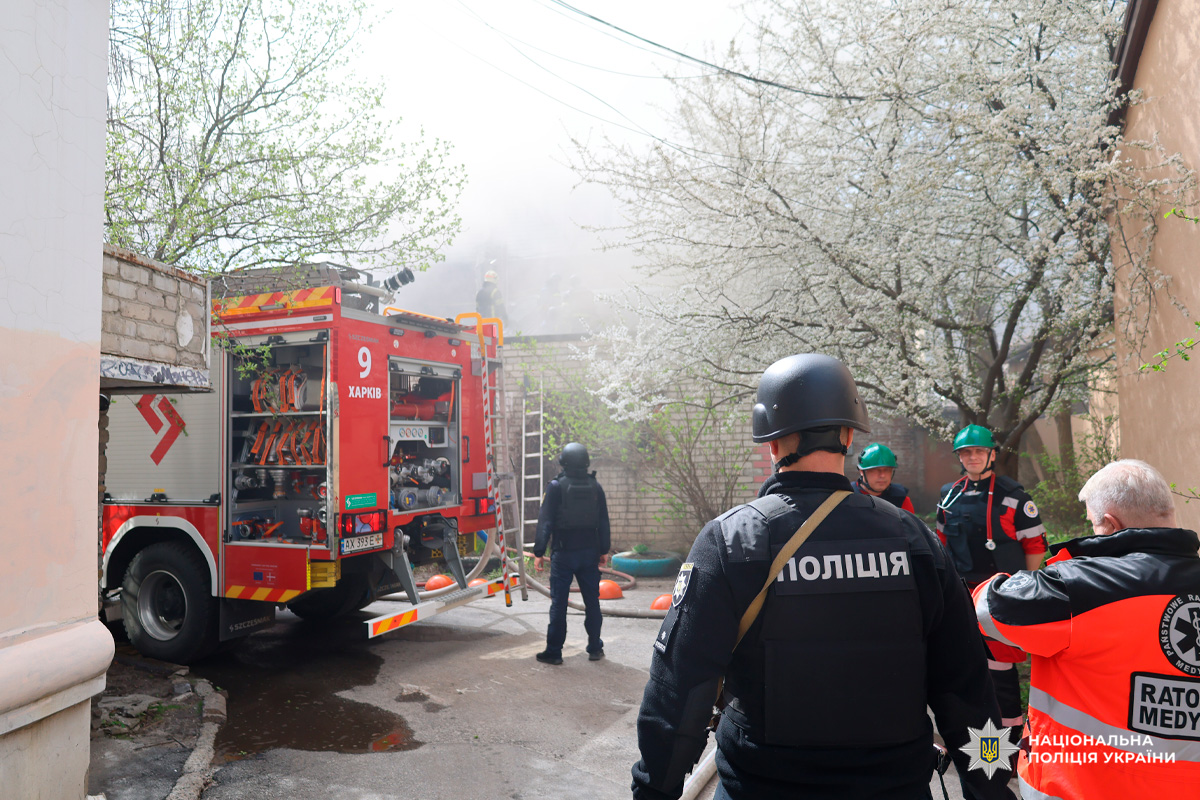 Спільні дії підрозділів поліції, пожежної служби та медичної допомоги під час ліквідації пожежі в Харкові. На місці працює пожежний автомобіль, поліцейські у захисному спорядженні та бригада медичного рятування.