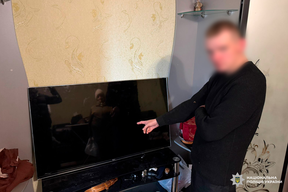 Особа вказує на вимкнений телевізор LG у кімнаті з орнаментальними шпалерами.