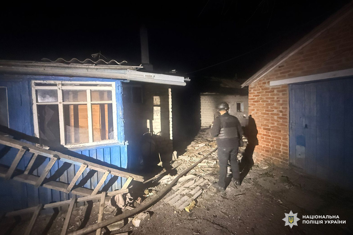 Пошкоджені житлові будівлі з уламками та руїнами, поліцейський у захисному спорядженні оглядає територію.