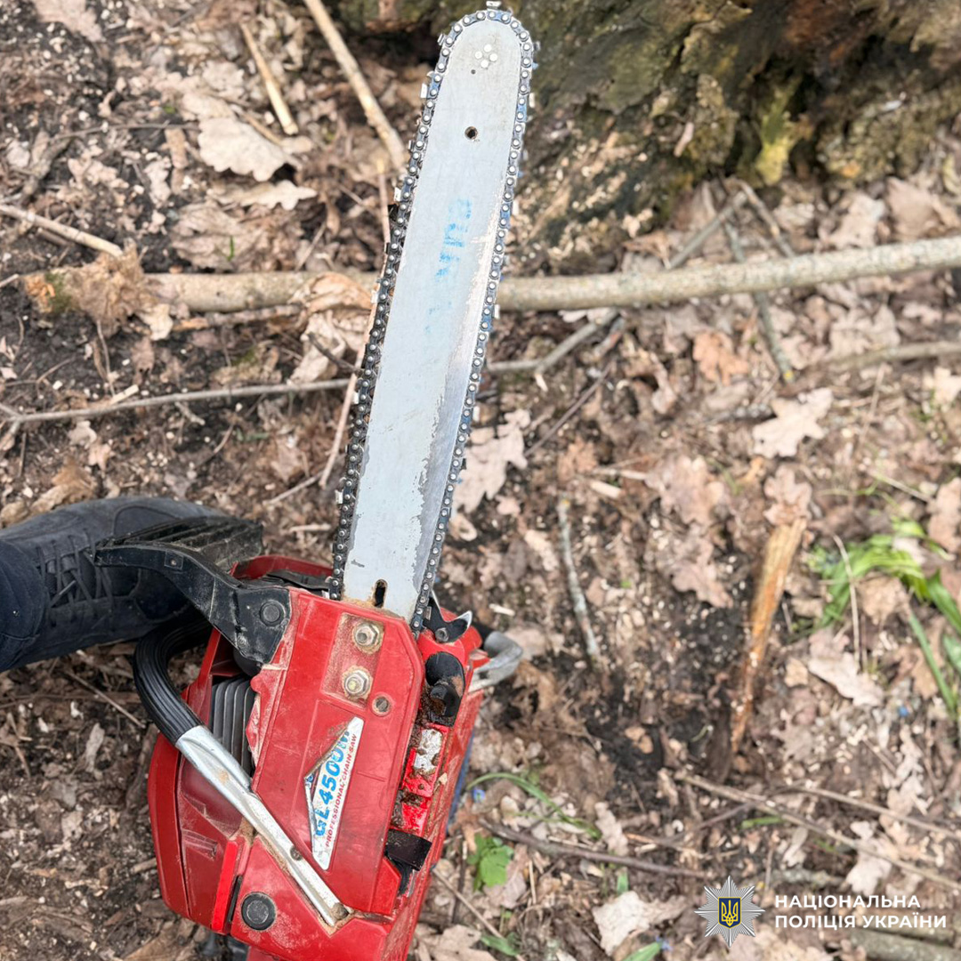 Червона бензопила з написом GL4500 лежить біля стовбура дерева серед сухого листя та гілок.