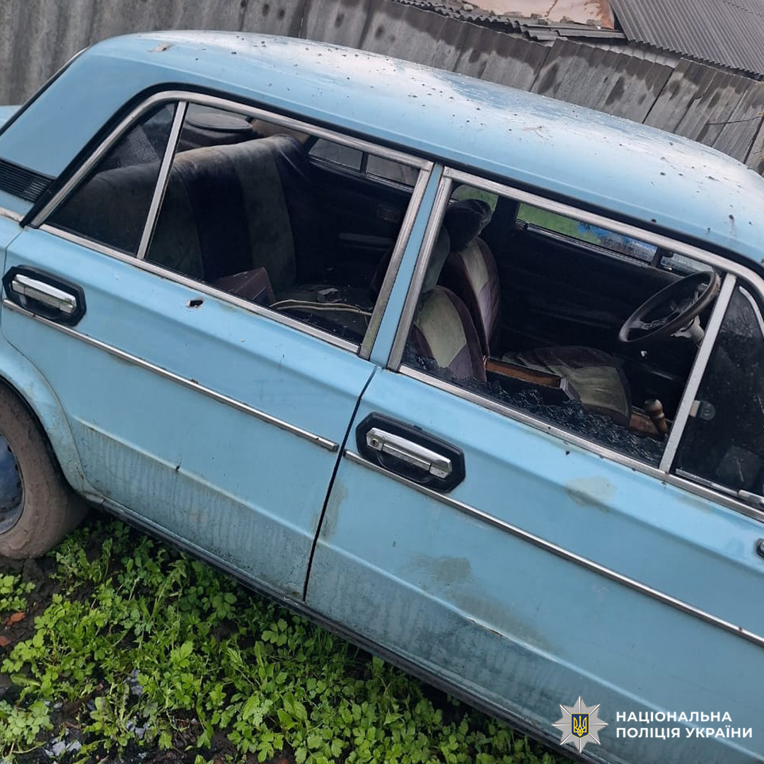 Пошкоджений легковий автомобіль світло-блакитного кольору з розбитими вікнами, припаркований біля металевої огорожі.
