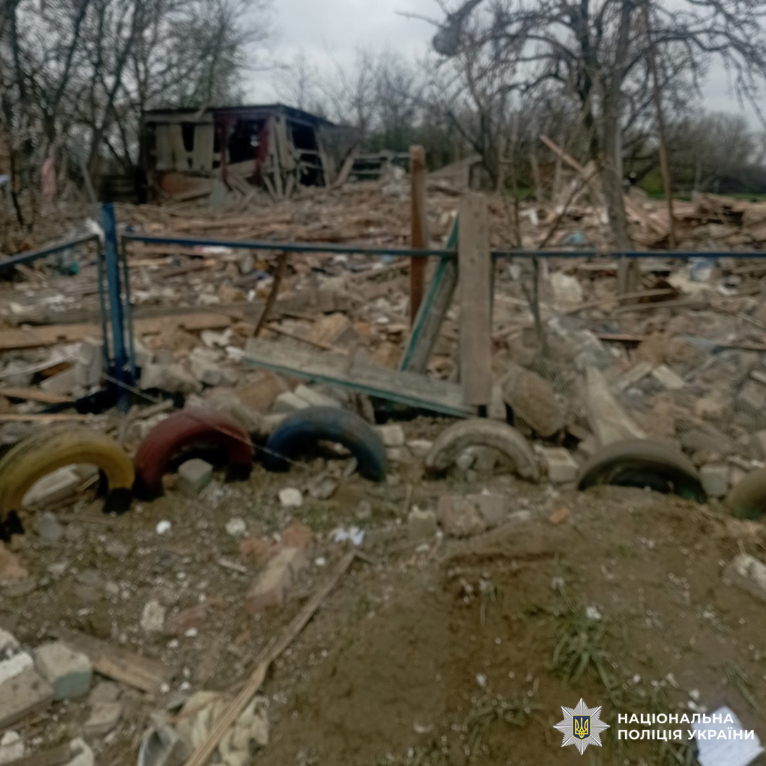 Зруйнована будівля з уламками дерева, цегли та металу, поруч огорожа з пофарбованими шинами.