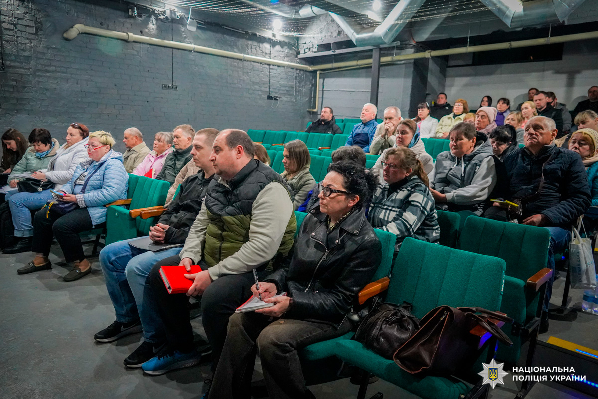 Учасники сидять у зелених кріслах аудиторії та слухають виступ.