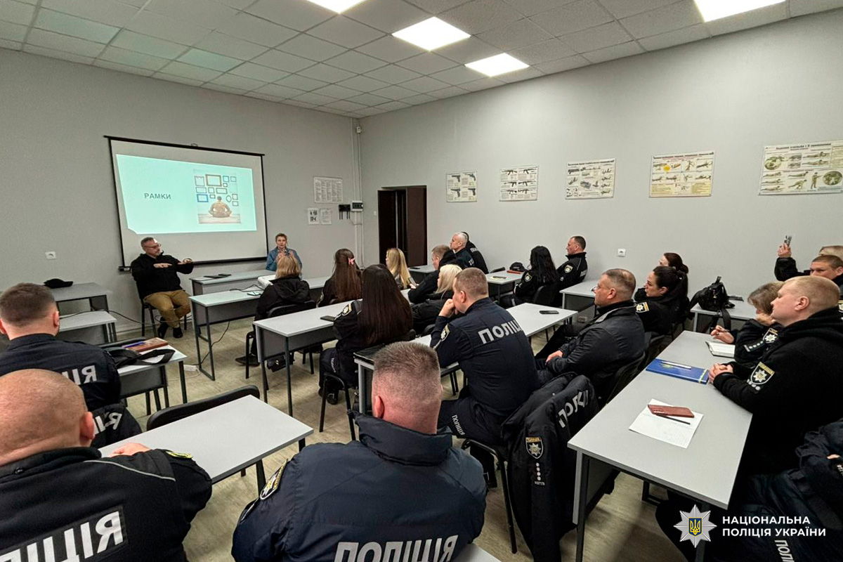 Поліцейські у формі сидять за партами та слухають презентацію в навчальній аудиторії.