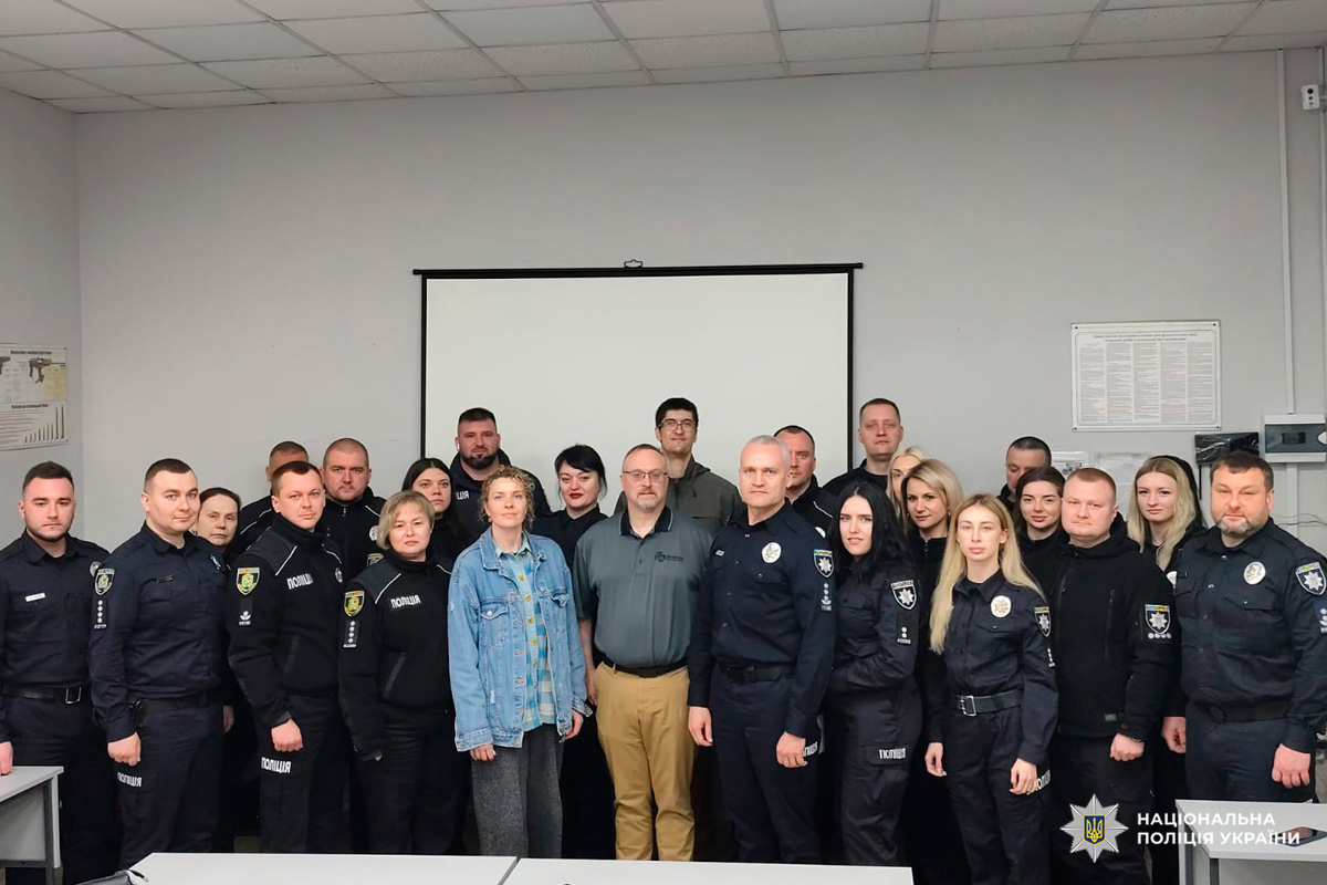 Група поліцейських у формі та цивільних осіб позує для фото в навчальній аудиторії.