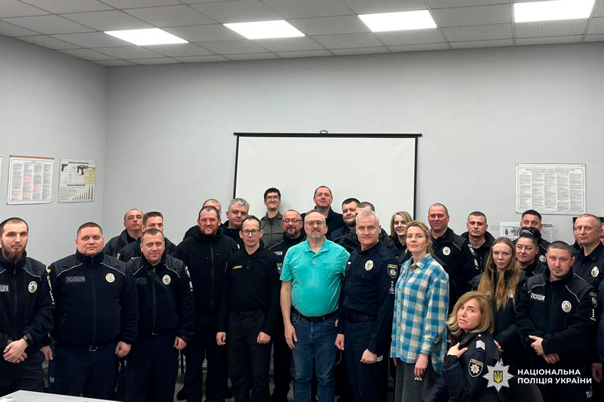 Група поліцейських у формі та цивільних осіб позує для фото в навчальній аудиторії.