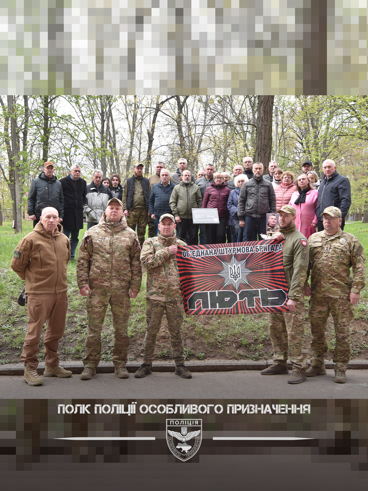 Група людей у військовій формі та цивільному одязі стоїть на алеї з банером “Об’єднана штурмова бригада Лють”.