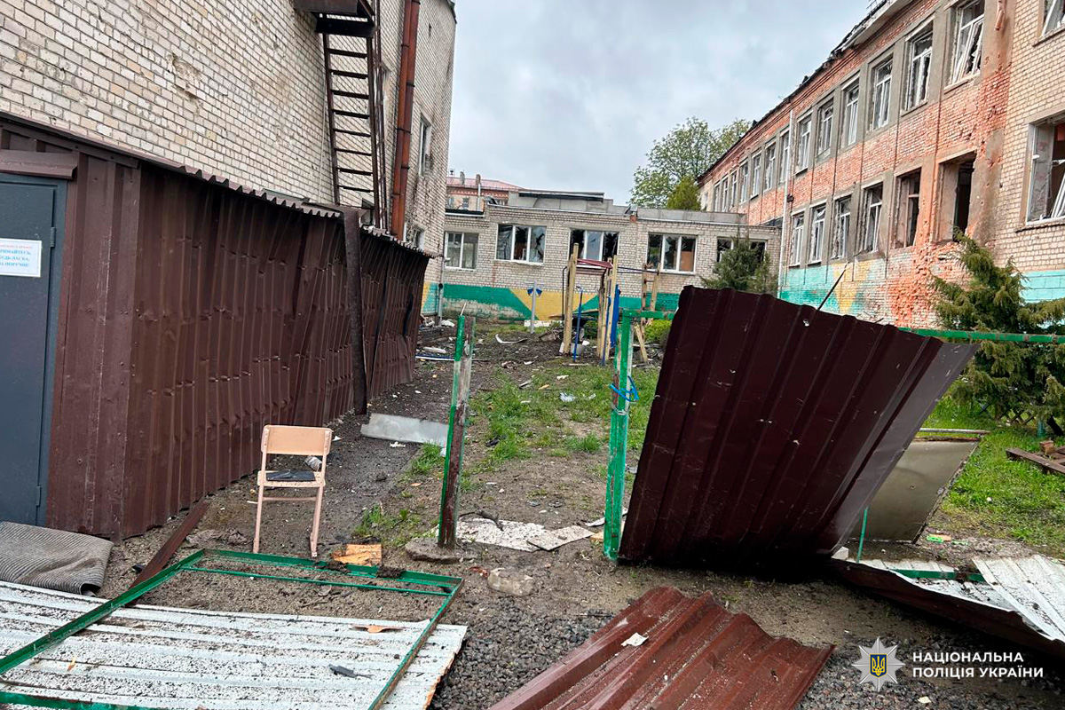 Зруйнована цегляна будівля з вибитими вікнами та уламками на подвір’ї.