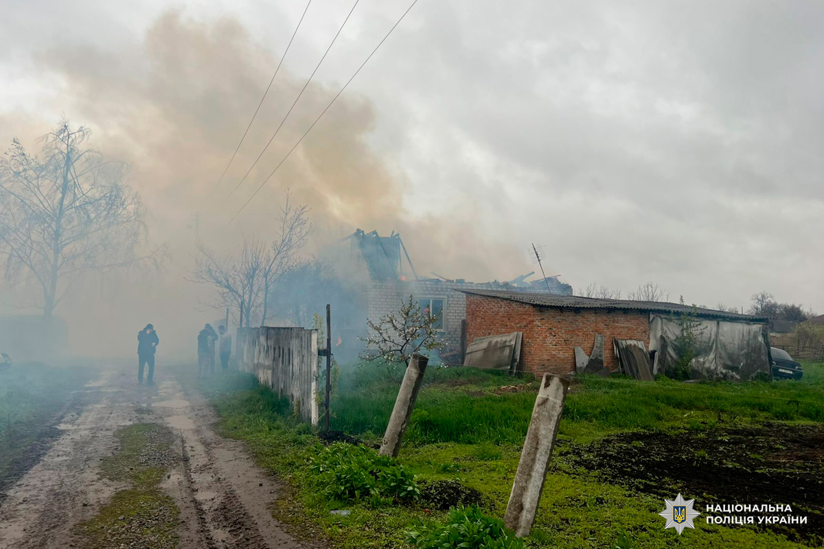 Пошкоджена цегляна будівля зі зруйнованим дахом і димом, поруч бетонні стовпи.