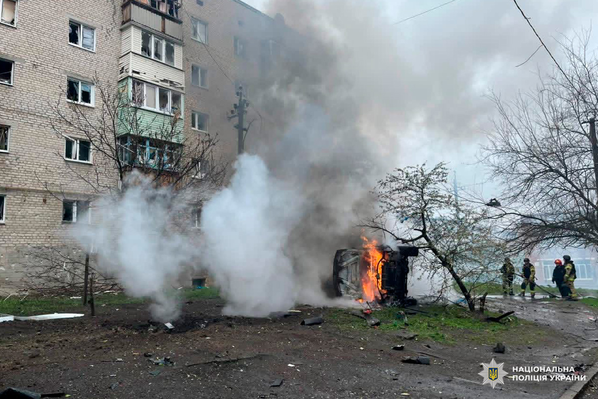 Палаючий перекинутий автомобіль біля багатоповерхівки, пожежники гасять вогонь.