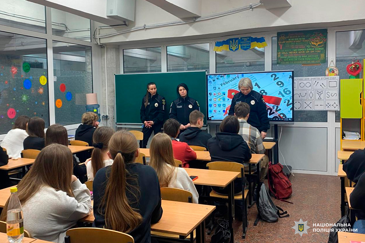 Класна кімната, де учні сидять за партами й слухають трьох поліцейських у формі, які стоять попереду та проводять презентацію.