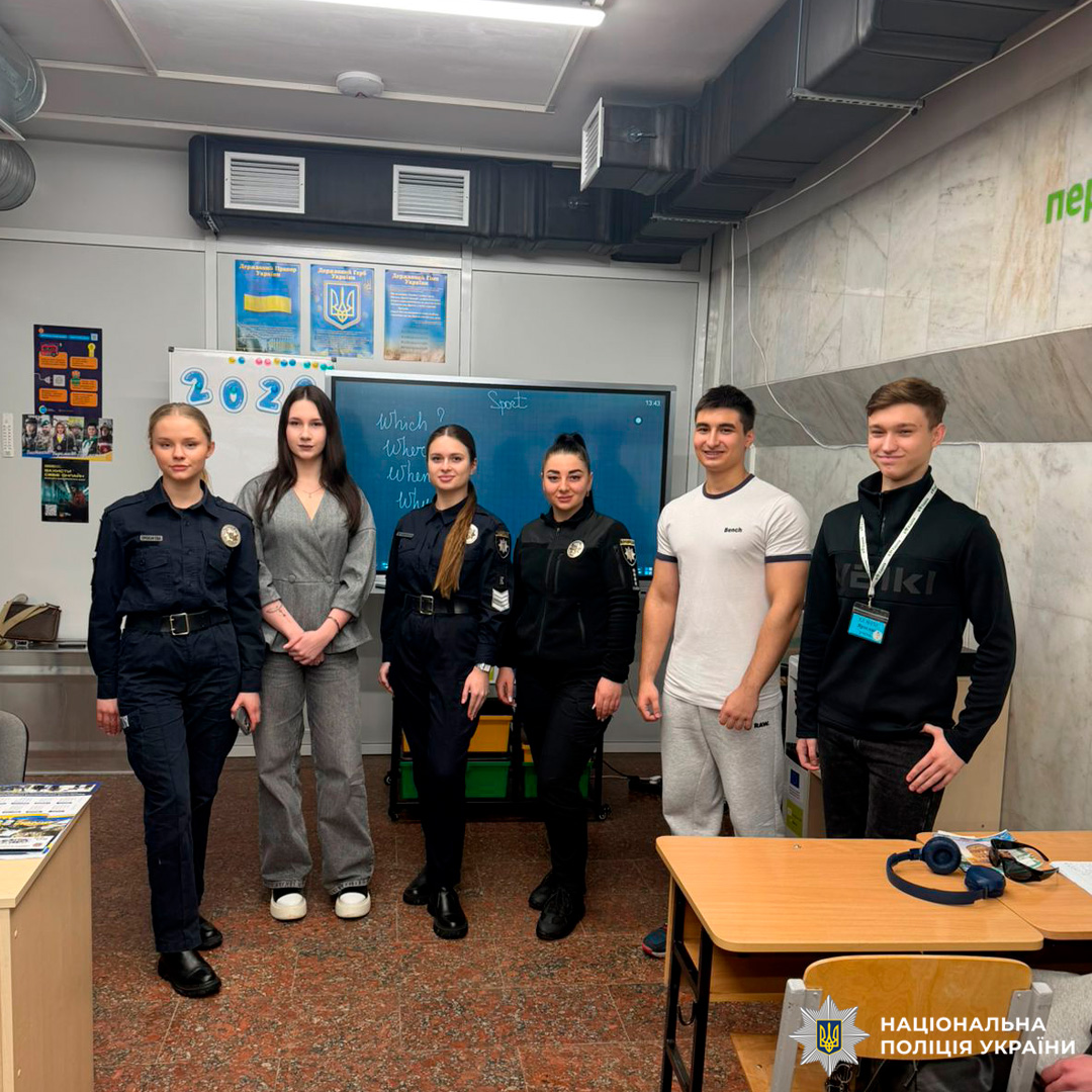 Шість осіб у класній кімнаті: троє поліцейських у формі з відзнаками, одна людина у сірому костюмі та двоє у повсякденному одязі.