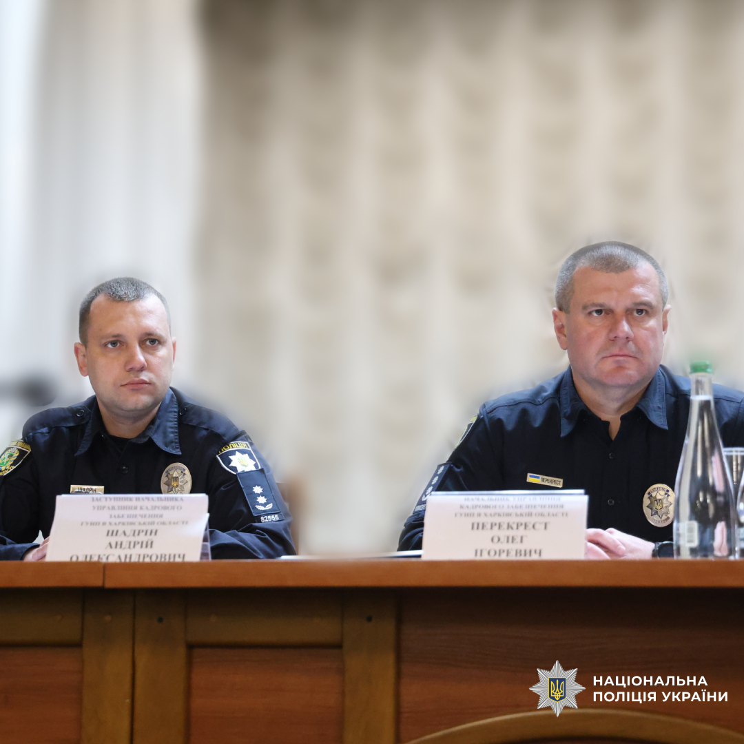 Двоє поліцейських у темній формі сидять за дерев’яним столом під час офіційної зустрічі чи конференції.