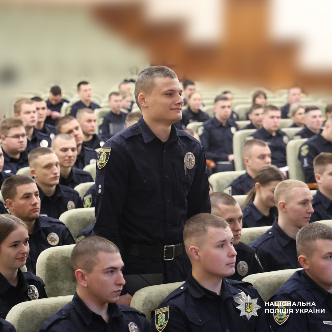 Велика група поліцейських у темній формі сидить у залі, схожому на лекційну або актову. Один із учасників стоїть у центрі, решта залишаються на місцях.