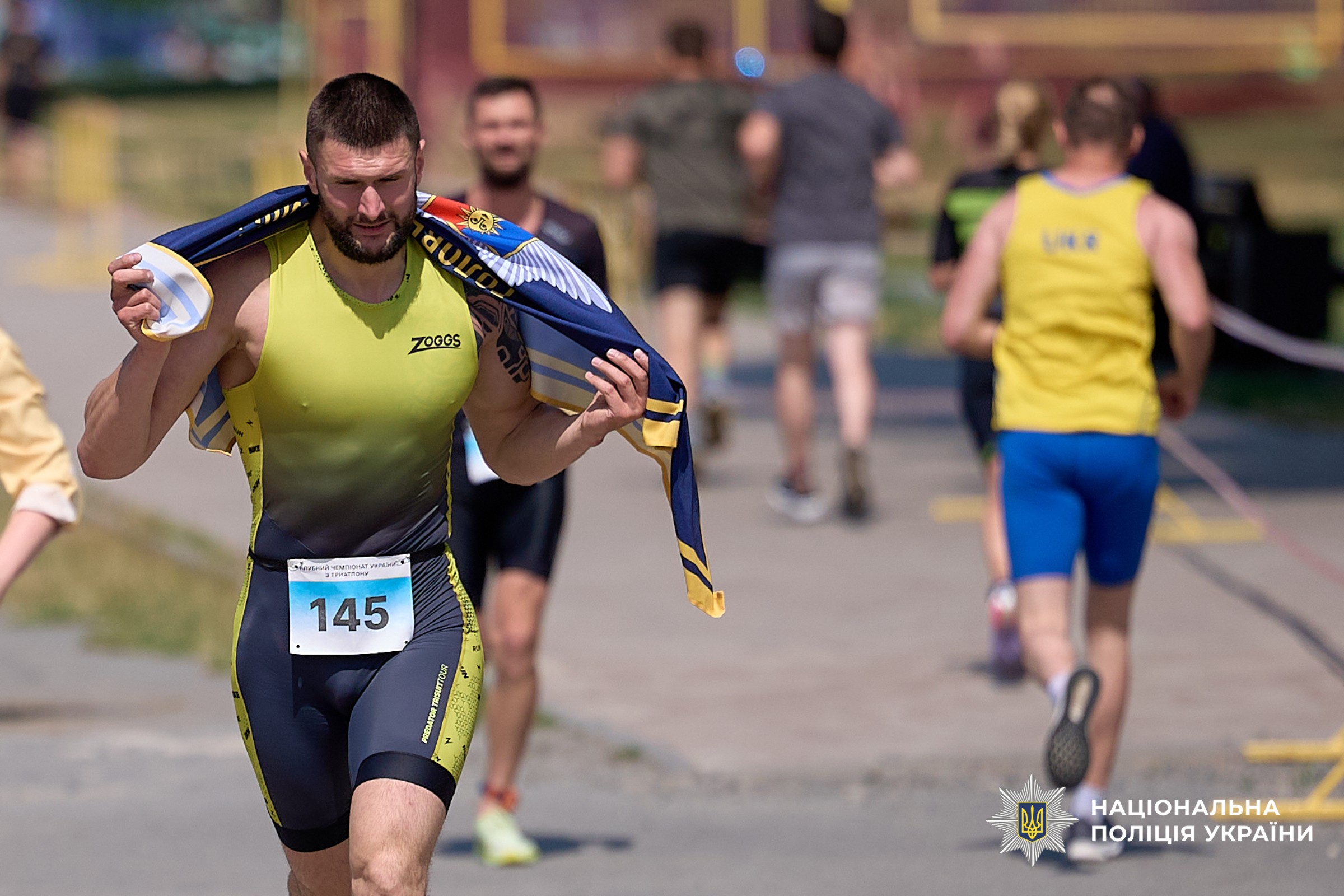 Поліцейський спецпризначенець, учасник команди у жовтій майці з прапором ГУНП за спиною долає 1,5 км дистанції з бігу