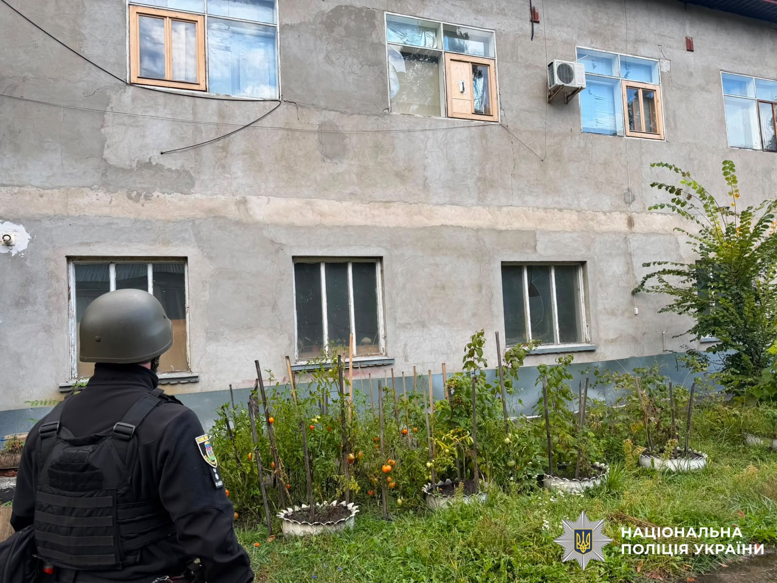 На фото пошкоджена будівля та працівник поліцїі, який документує наслідки атаки рф.