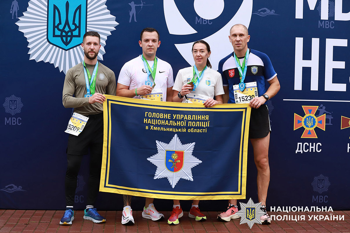 Четверо поліцейських, серед яких срібна призерка Каріна Рибак, на фоні банера з надписом "МВС незламні" тримають прапор з надписом "ГУНП в Хмельницькій області"