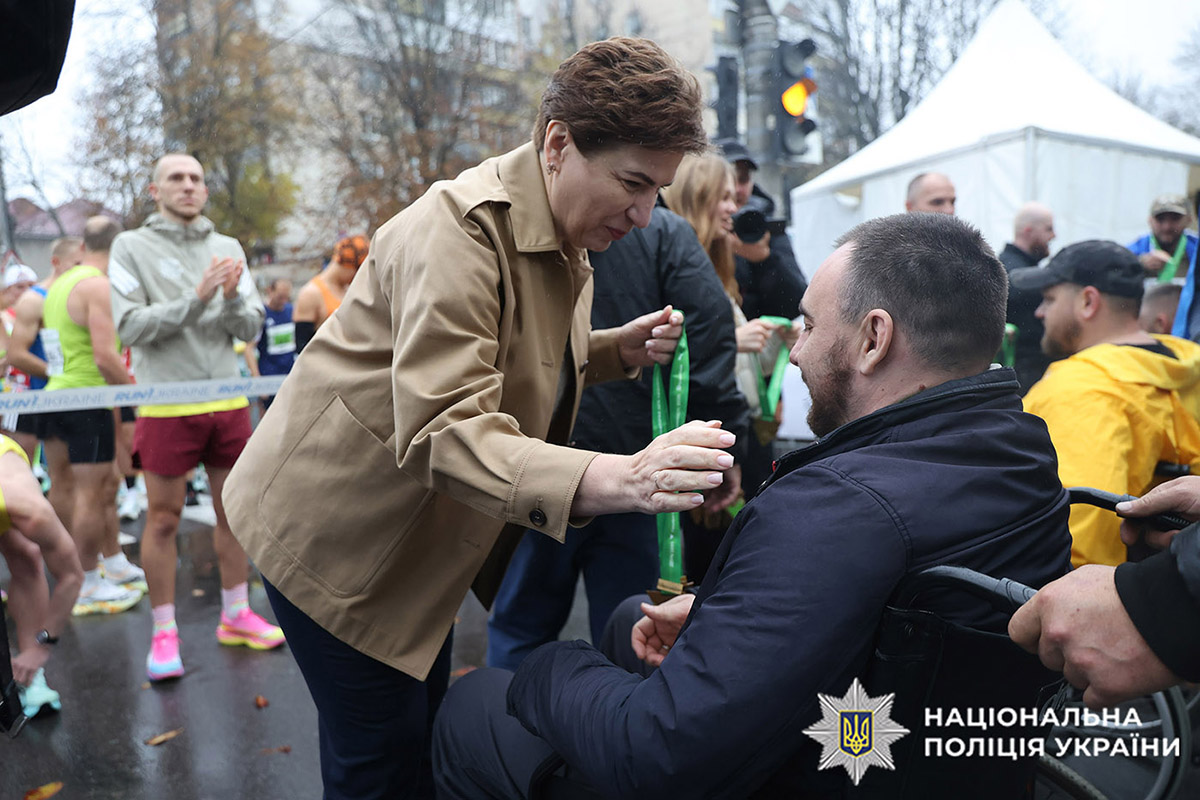 Державний сектерар МВС України Інна Ящук одягає медаль учасника забігу на шию ветеранові, який сидить у кріслі колісному