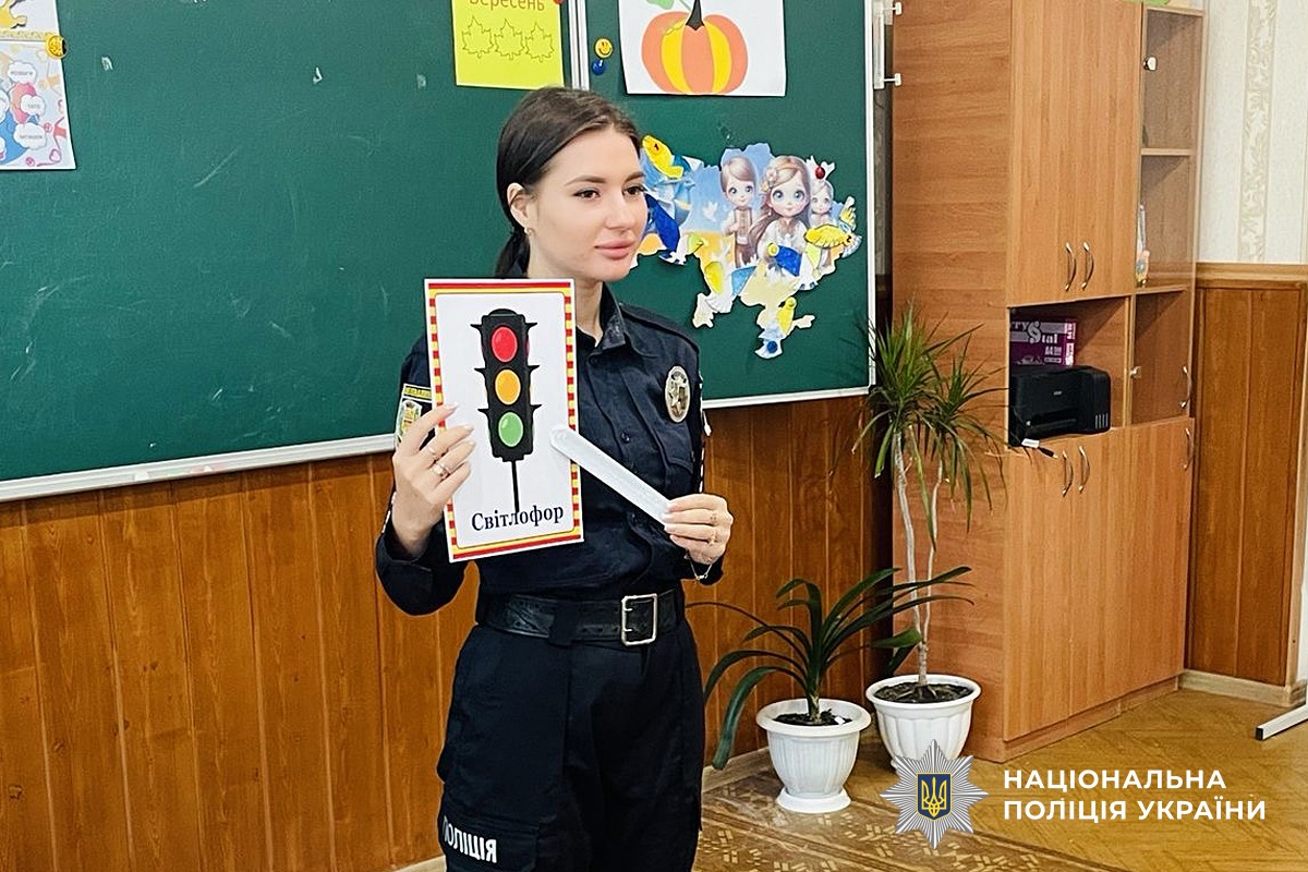Поліцейська демонструє школярам світлофор