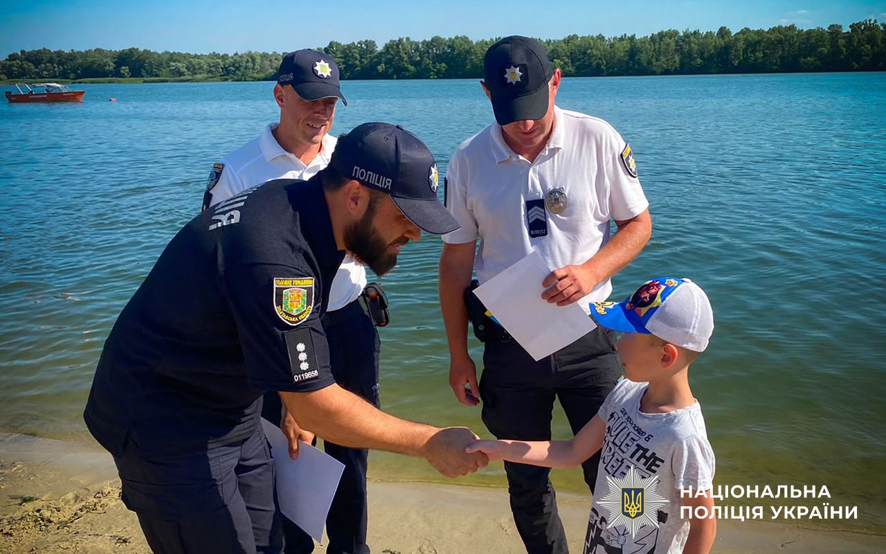 На березі Дніпра водний поліцейський спілкується з дитиною про правила безпеки на воді