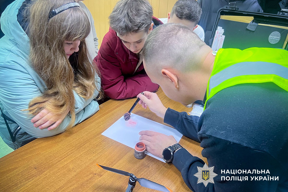 поліцейський показує,  як відбирають зразки пальців рук 