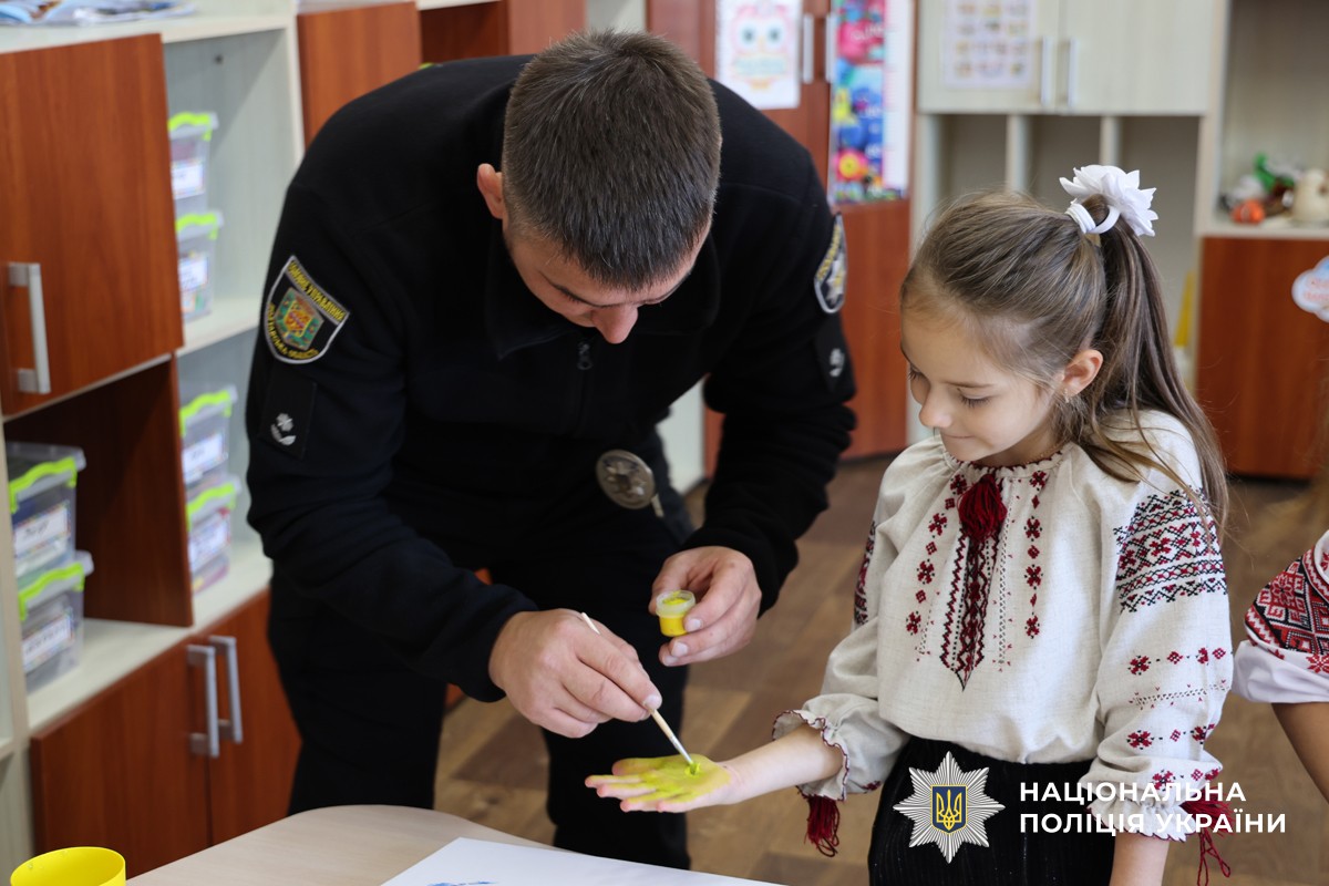 Поліцейський фарбує дівчинці руку у жовтий колір