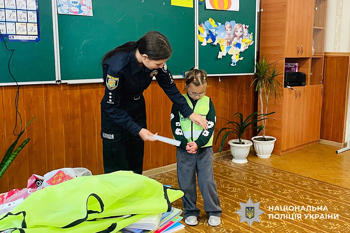 Поліцейська прикріпляє на одяг дитині світловідбивний елемент