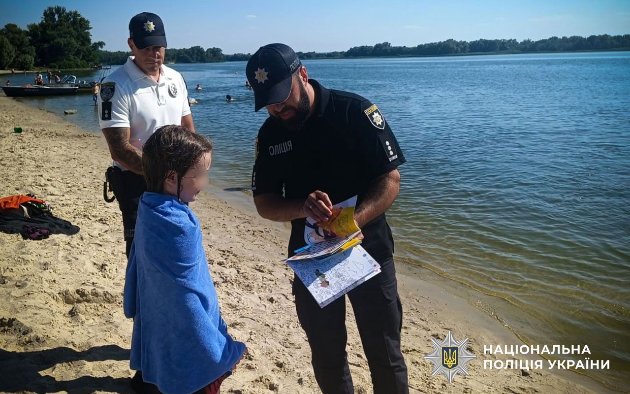 На березі Дніпра водний поліцейський спілкується з дитиною про правила безпеки на воді