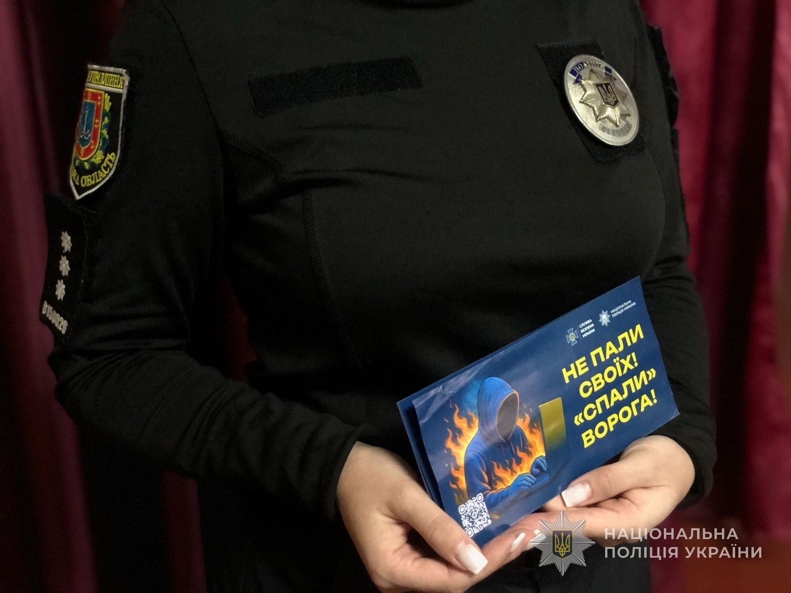 Поліцейська тримає в руках спонукаючу листівку: "Не пали своїх! "спали" ворога!"