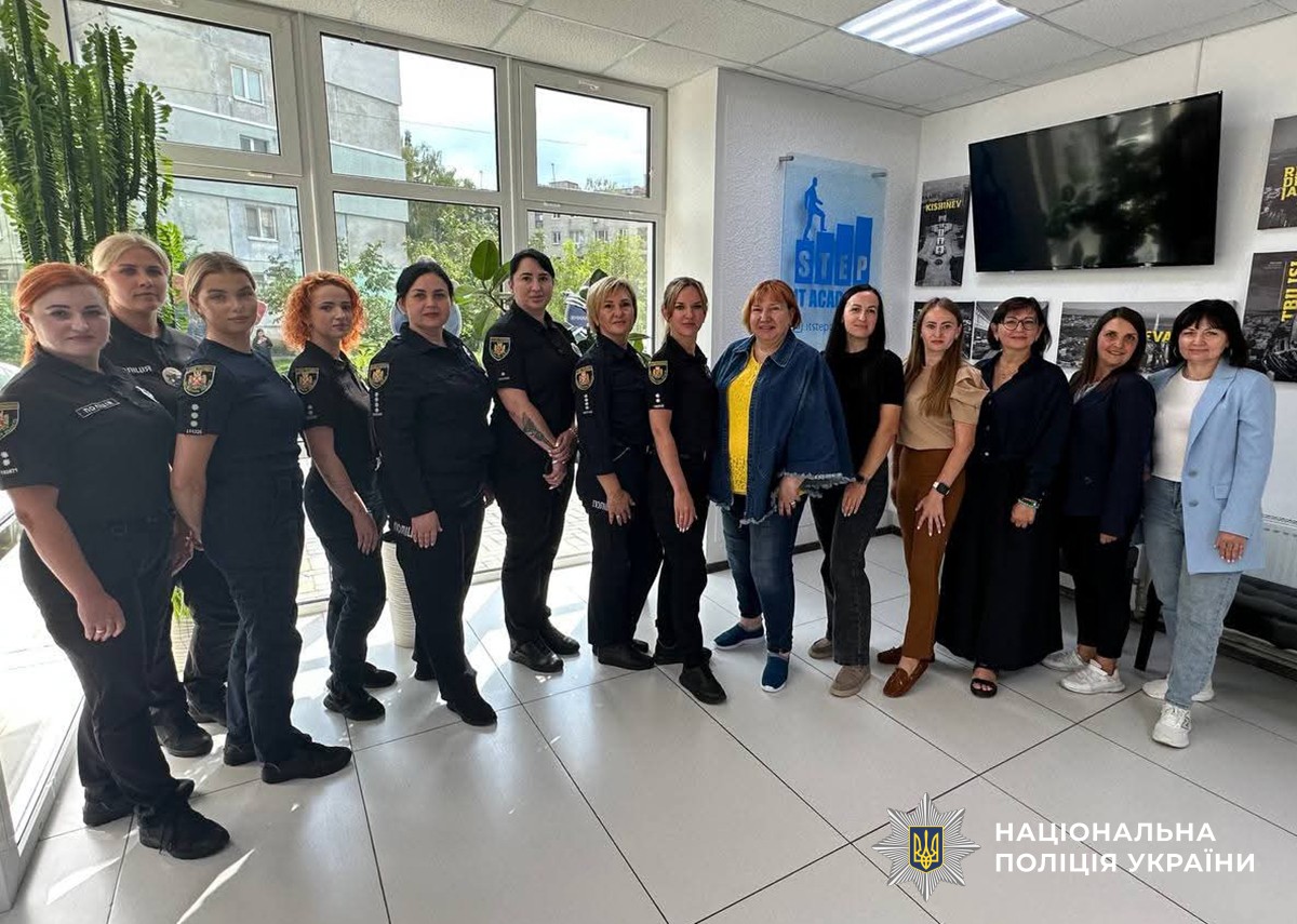 Група жінок у поліційній формі та цивільному одязі стоять разом у світлому приміщенні, позують для спільного фото