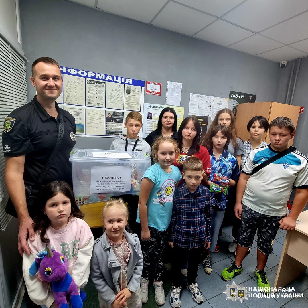 поліцейський та група дітей у приміщенні біля скриньки для збору допомоги.