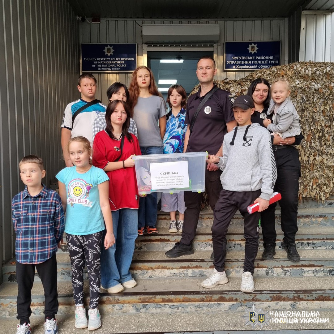 поліцейський та діти біля відділу поліції з прозорою скринькою для допомоги.