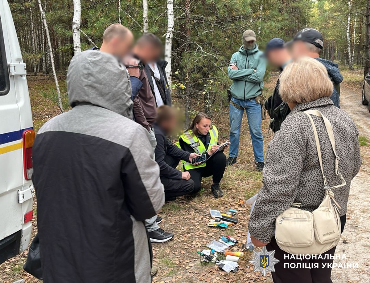 На землі лежать особисті речі чоловіків які намагалися виїхати за межі кордону, слідча та співробітник СБУ присіли та описують їх. навколо них стоять поняті, співробітники СБУ та причетні