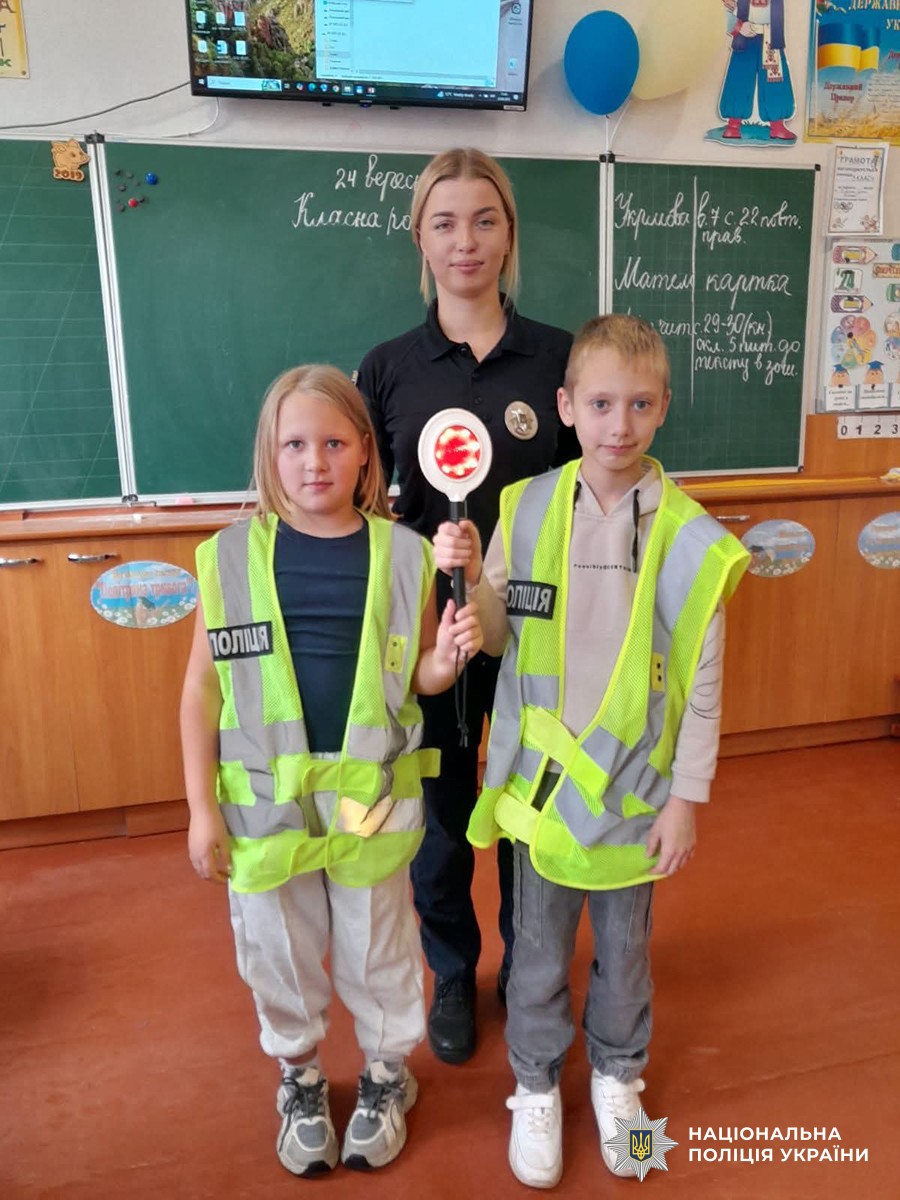 Поліцейська та двоє дітей у світловідбивних жилетах у навчальному класі
