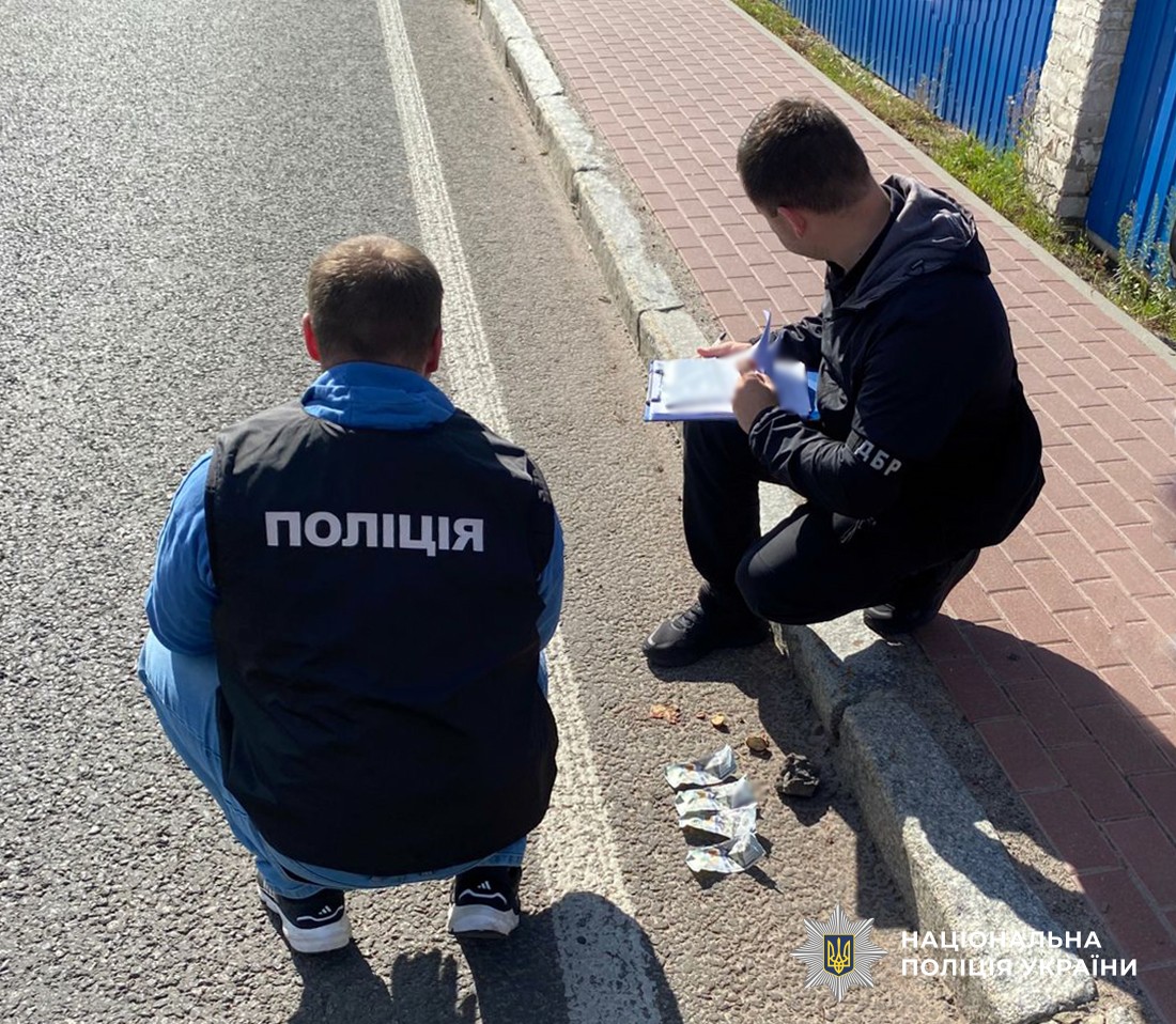 Поліцейський та працівник ДБР присіли. Біля них на асфальті лежать 5 доларових купюр.