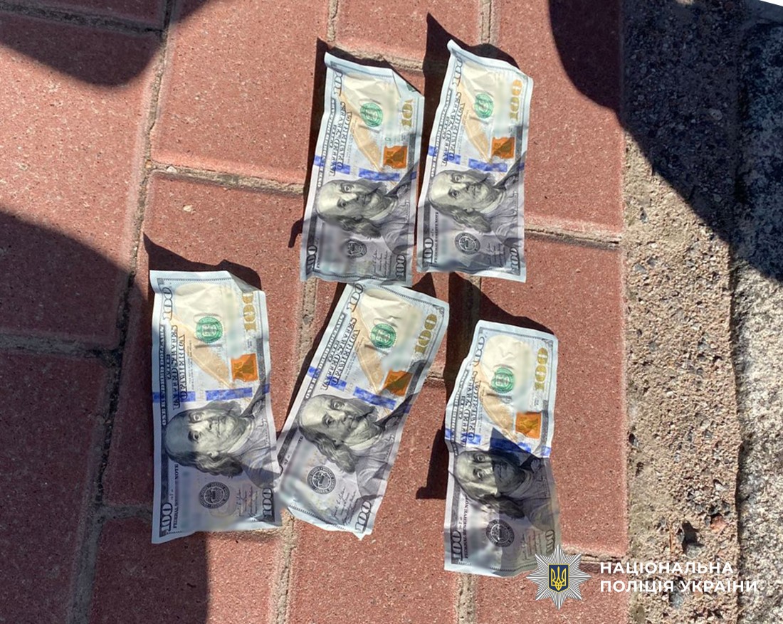 5  купюр номіналом по 100 доларів лежать на асфальті.