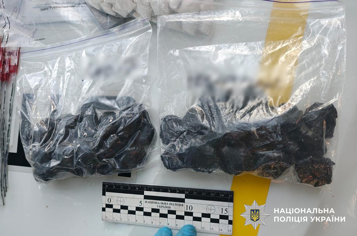 невеликі згортки чорного кольору у двох зіп-пакетах лежать на поліцейському авто. рука криміналісти в рукавичці тримає криміналістичну лінійку