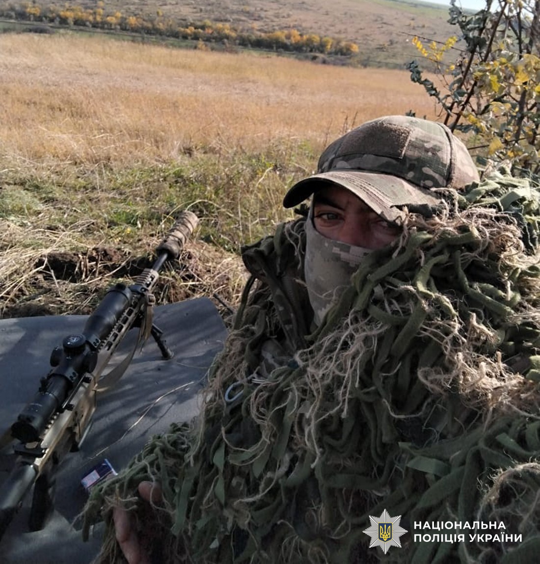 Герой на позиції в спеціальному маскувальному костюмі. Поряд снайперська гвинтівка