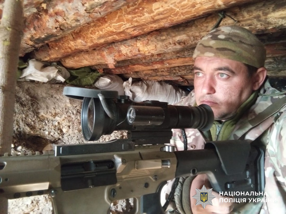 Руслан у бліндажі прицілюється з гвинтівки.