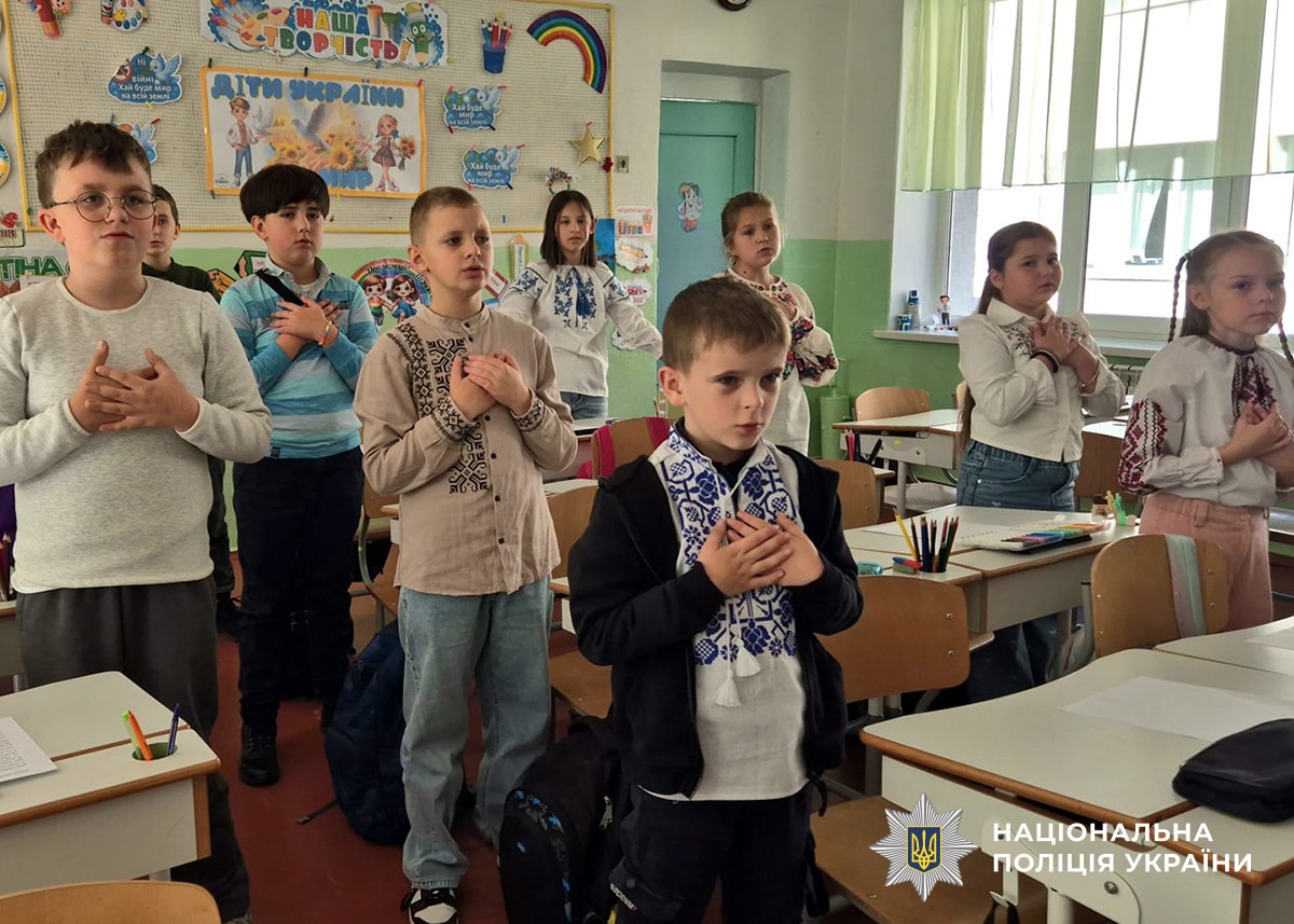 діти стоять біля своїх парт, тримають руки в себе на грудях і співають