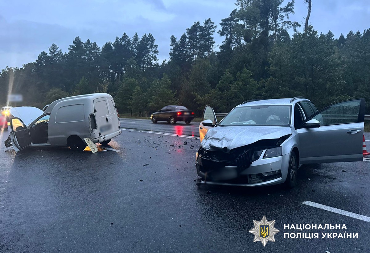 Справа видно сріблясту Skoda з пошкодженою передньою частиною, дверцята відчинені. Зліва  білий фургон ЗАЗ, що стоїть боком, також із сильно розбитою передньою частиною. На дорозі багато уламків після зіткнення.