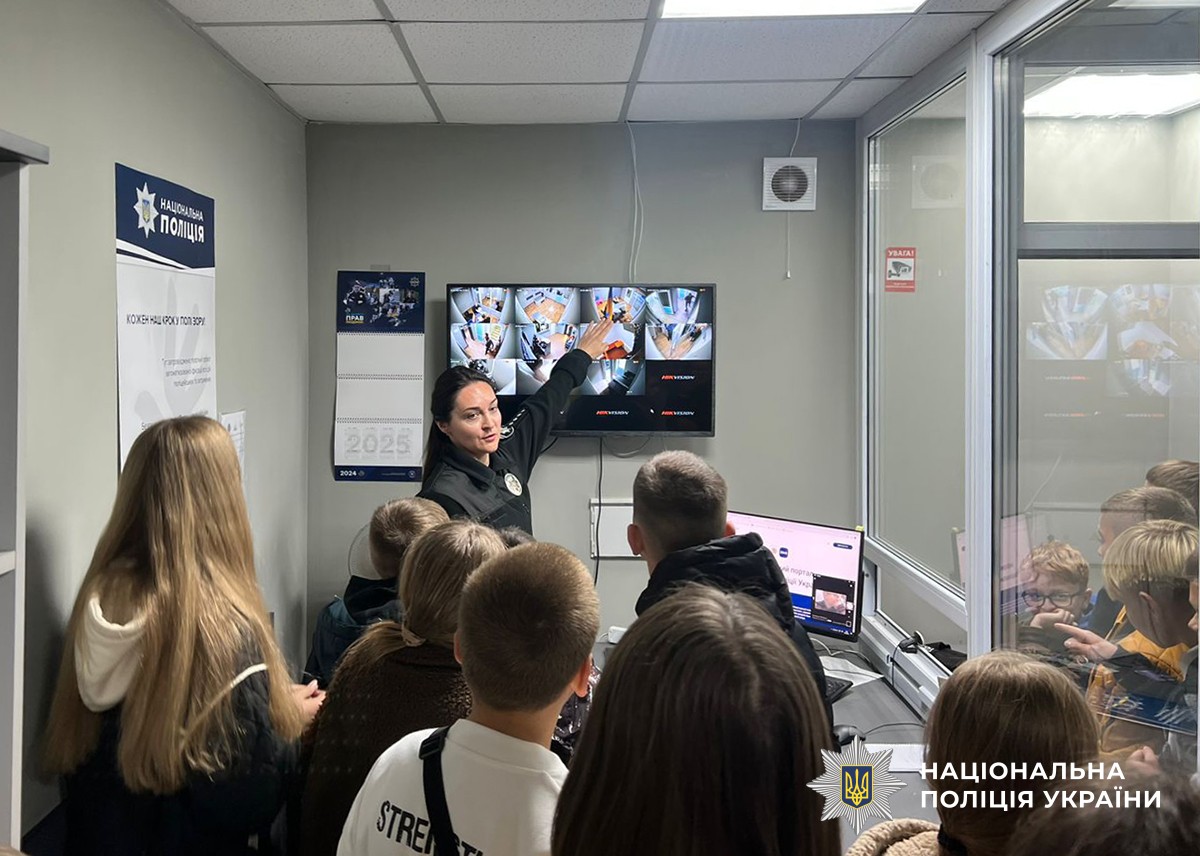 Поліцейська показує дітям камери відеоспостереження, виведені на екран.