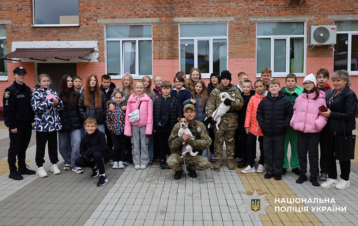 На подвір'ї ліцею на спільному фото позують група дітей, поліцейські кінологи зі службовими собаками