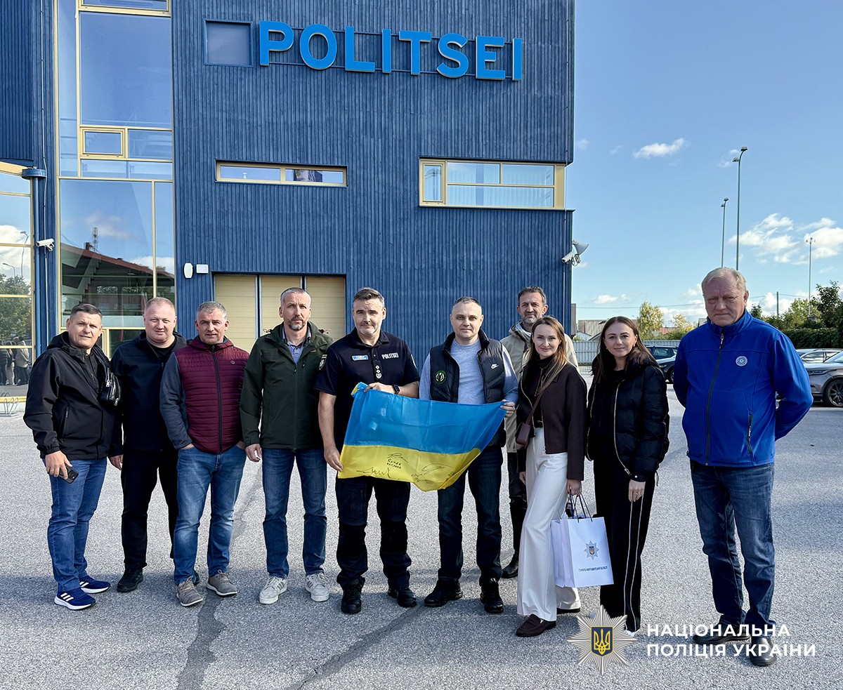 Поліцейські ГУНП в Житомирській області разом з естонськими колегами стоять біля відділку поліції. В руках тримають прапор України.