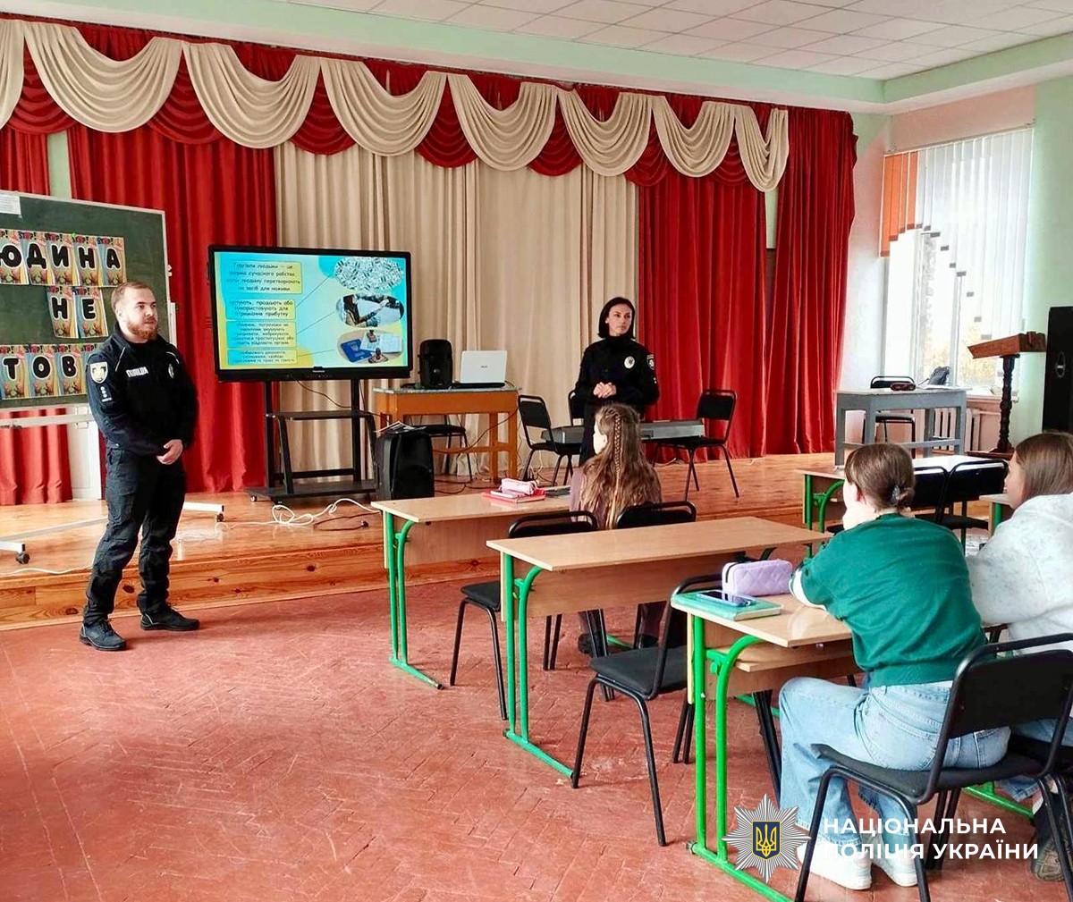 Поліцейський та поліцейська в актовій залі розповідають щось дітям
