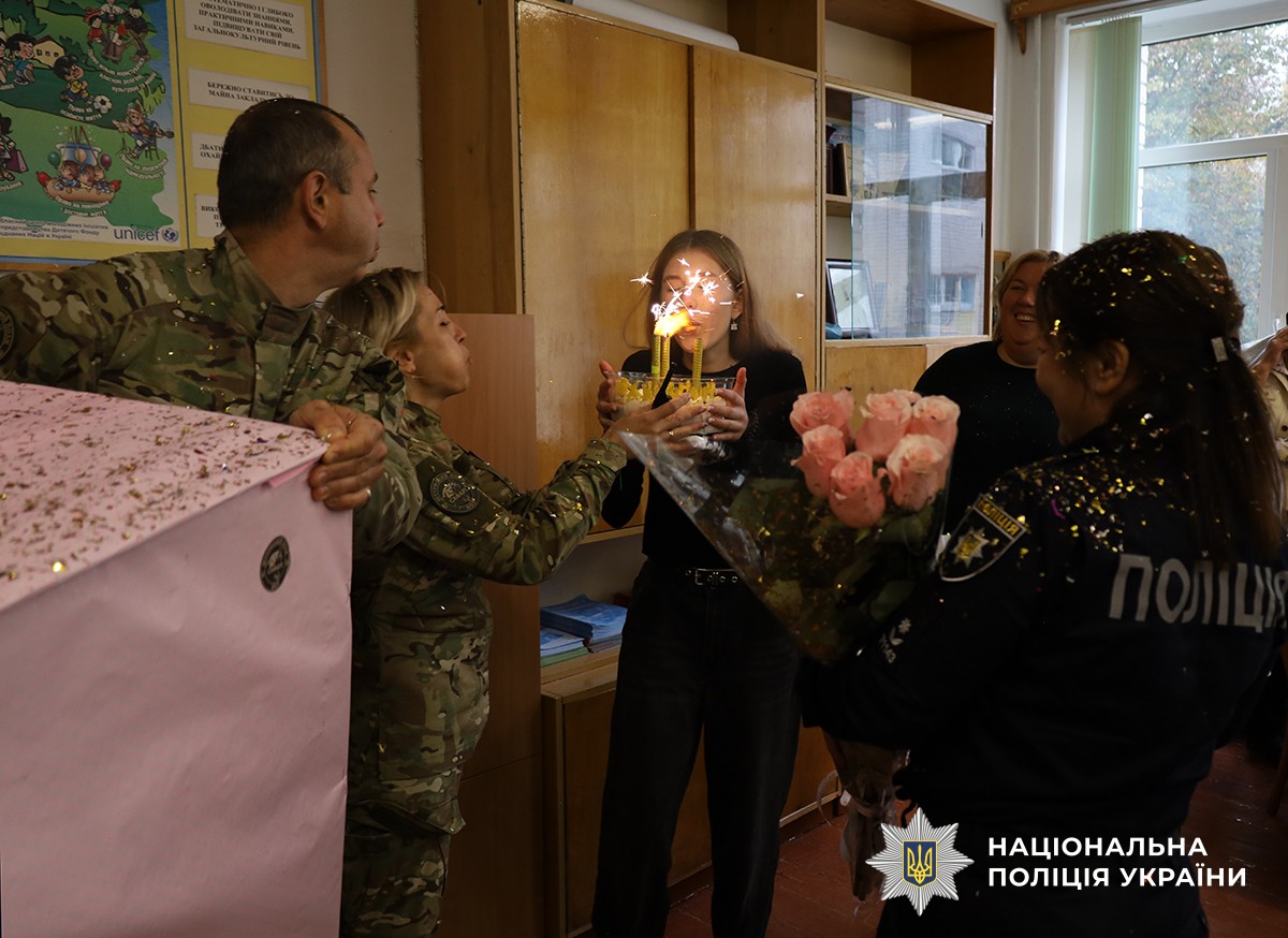 Зліва в кадр потрапив поліцейський у комуфляжі який тримає рожеву коробку. Поруч поліцейська у камуфляжі тримає торт. У центрі іменинниця, поряд із якою стоять поліцейська з квітами та подарунками та вчителька. Усі разом вони задувають свічку на торті.
В повітрі літають блискітки від хлопавки.